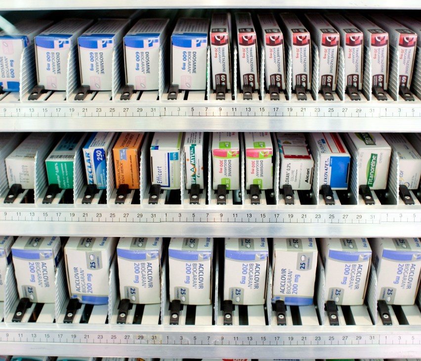 Organized shelves of white, blue, and colored medication pill boxes with numbered compartments in a pharmacy display.