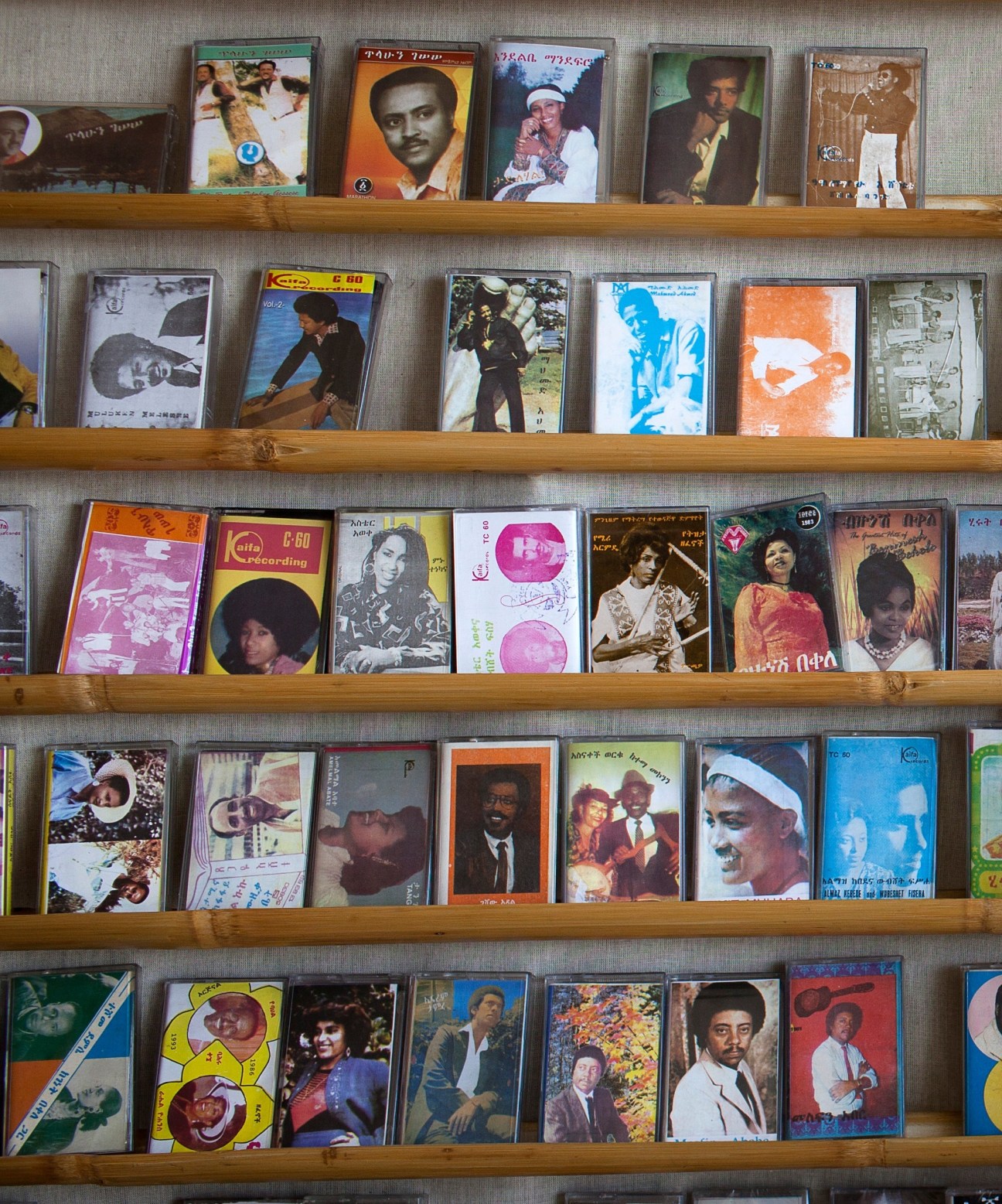 Wooden shelves displaying vintage Ethiopian music cassettes with colorful covers and Amharic text.
