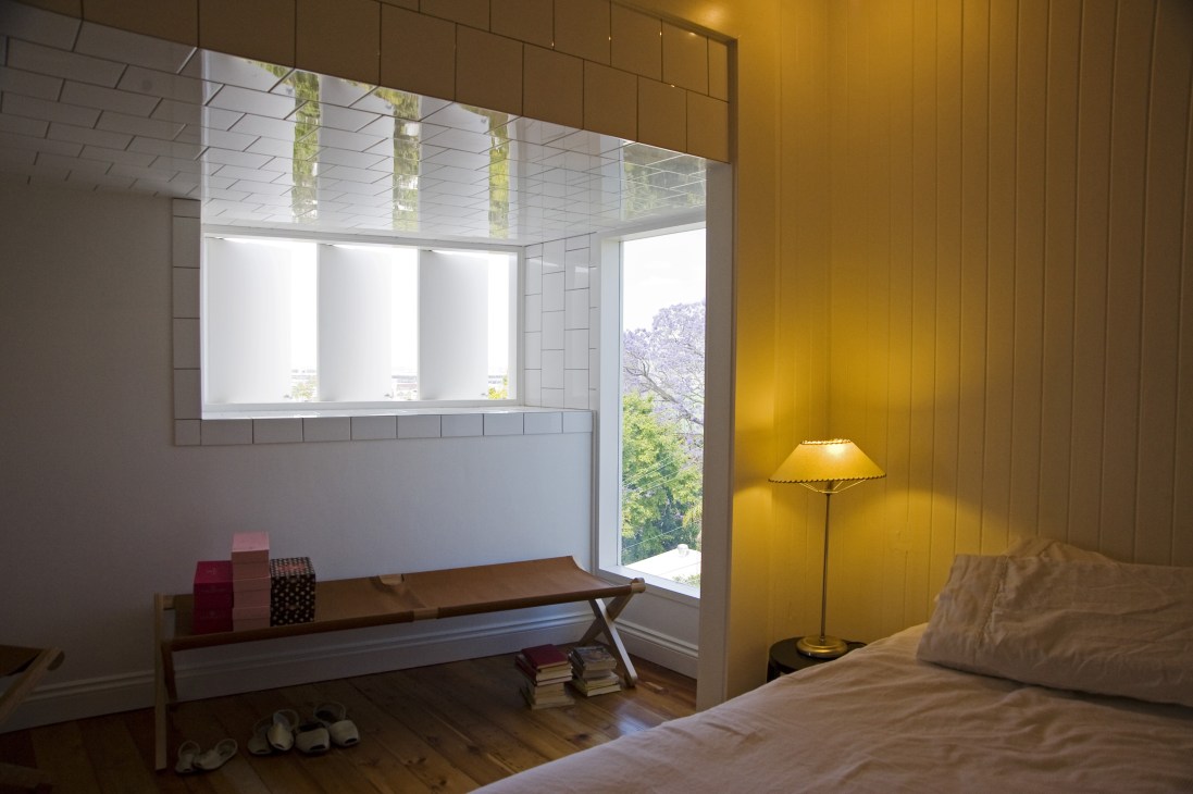 Bedroom with yellow-painted walls, wooden day bed, and large windows overlooking Brisbane.