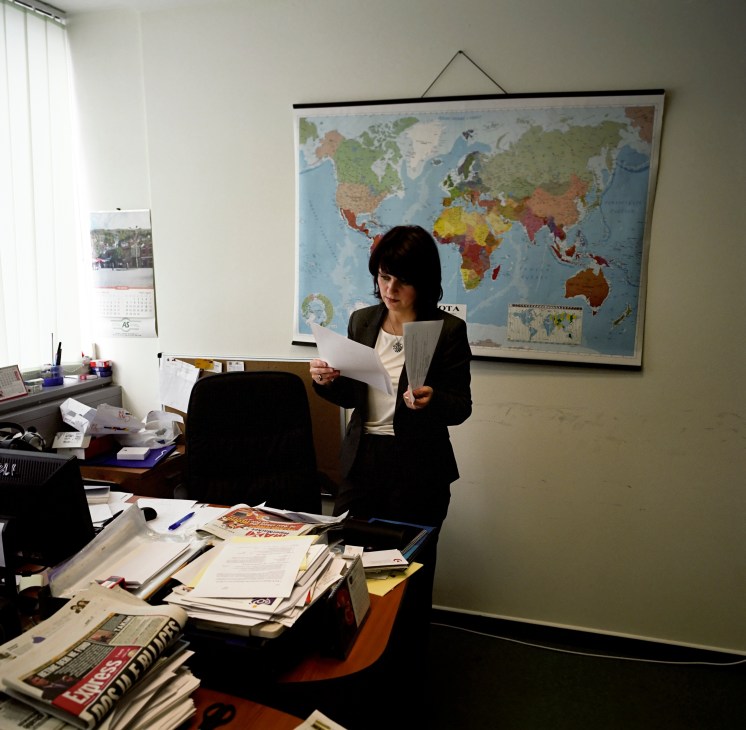 Venera Llunji, a political adviser at Kosovo's foreign affairs ministry, standing in an office holding documents with a world map on the wall behind her.