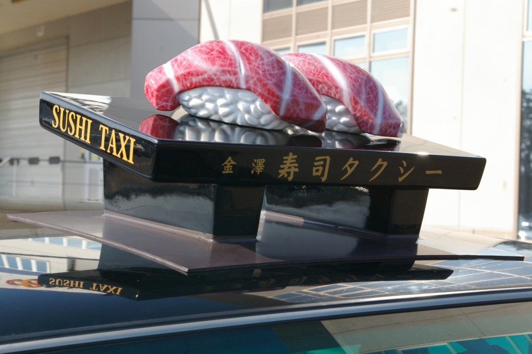 Sushi Taxi roof ornament featuring model fatty tuna on sushi tray with Japanese characters and signage on vehicle.