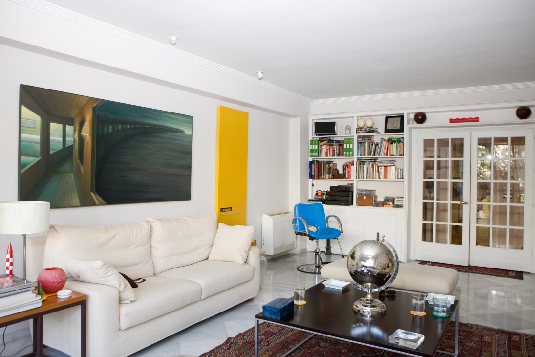 Modern living room with white sofa, artwork, shelving, and contemporary furnishings.