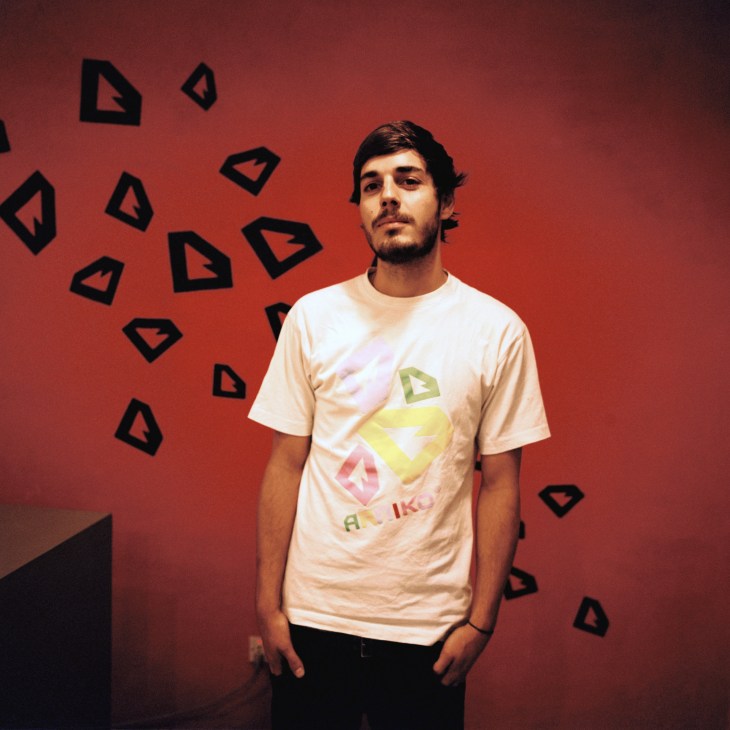Man wearing cream-colored t-shirt with geometric design against red wall with black triangle shapes.