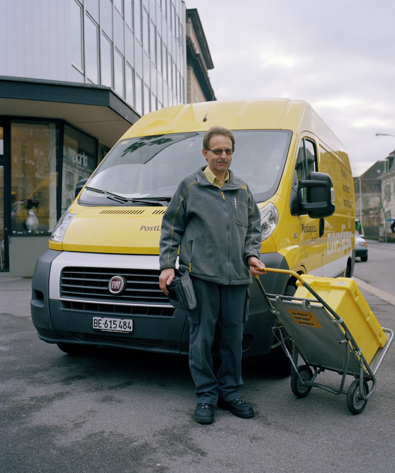 Herr Zwahlen, a Swiss Post parcel delivery man, stands in front of a yellow PostLogistics van in Bern.