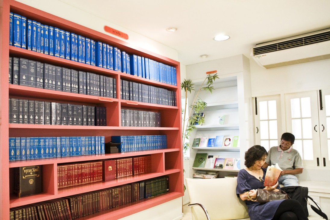 Two people browsing books in a library with a large red shelving unit filled with Buddhist texts and volumes.