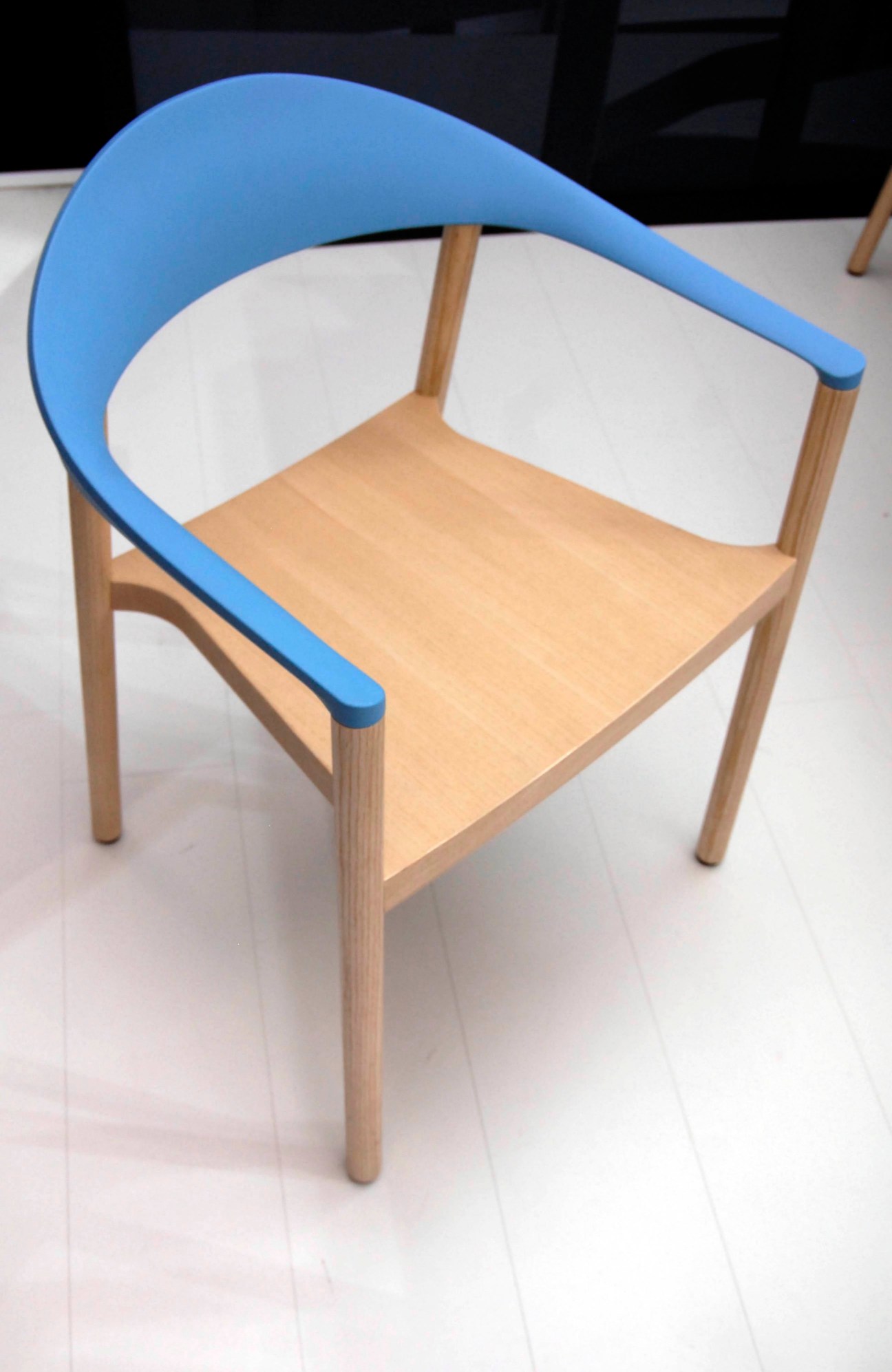 Monza chair for Plank by Konstantin Grcic featuring a blue curved backrest and wooden seat.