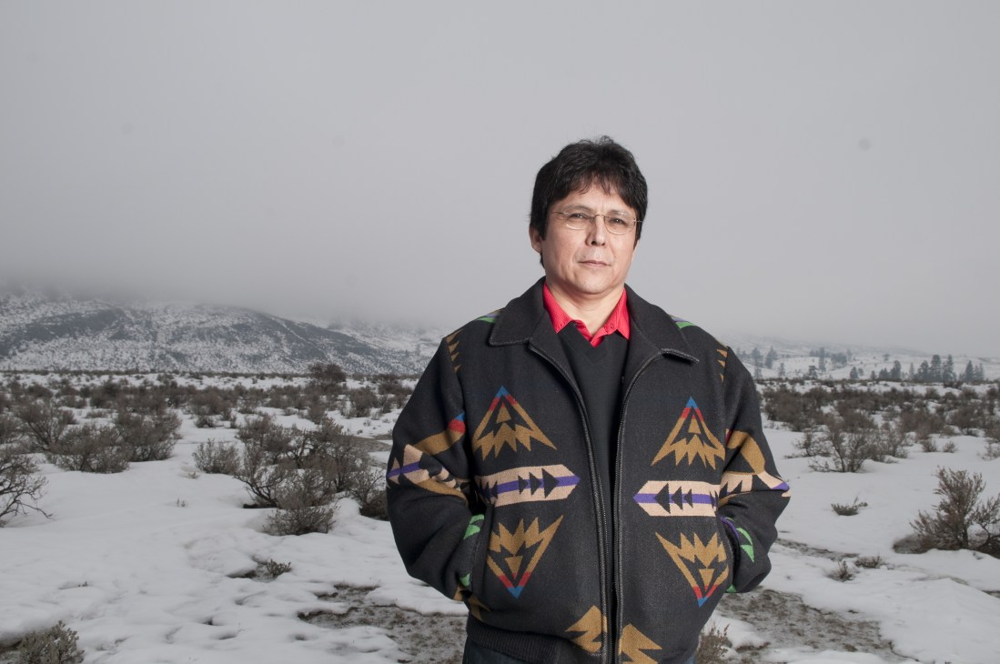 Chief Clarence Louie standing in snowy grassland wearing a black jacket with colorful geometric patterns.