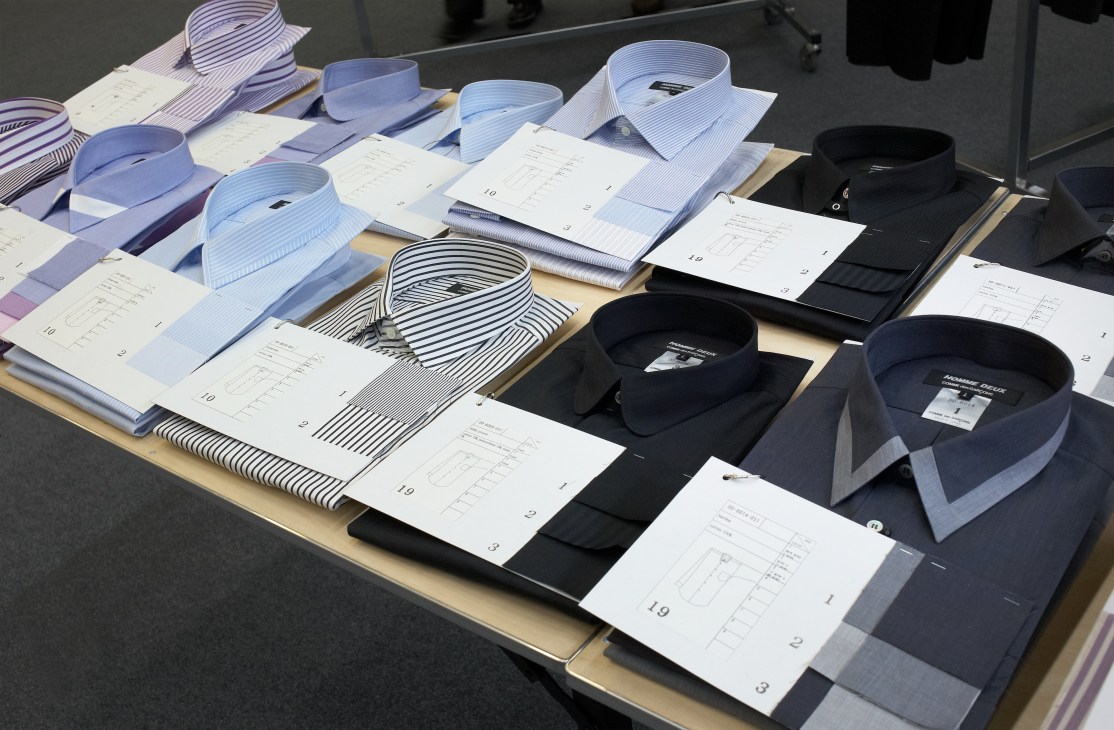 Display of folded dress shirts in various colors and stripe patterns with size labels at a menswear trade show.