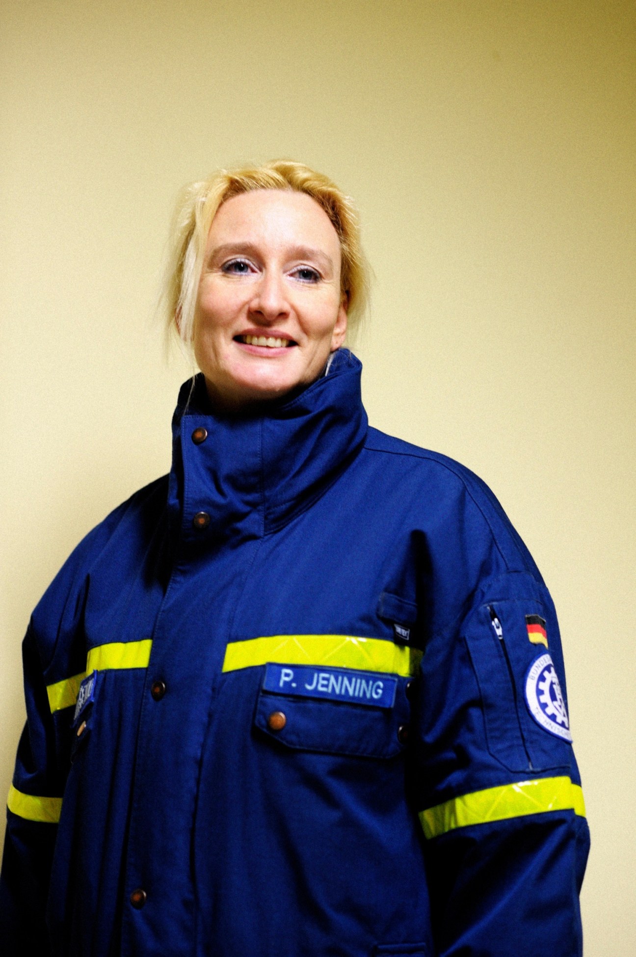 Woman in blue THW uniform with yellow reflective stripes and name badge P. Jenning smiles at camera.