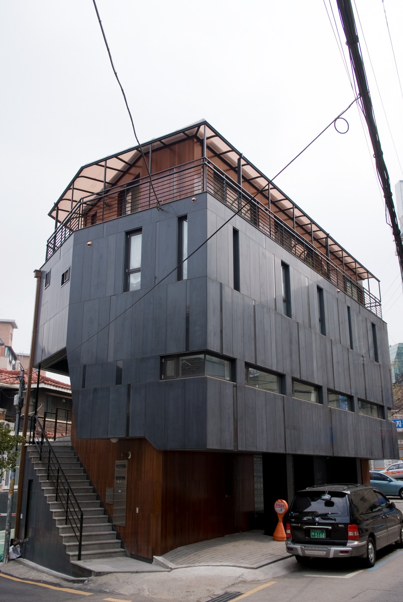 Modern apartment building in Shinsa-dong with dark metal cladding, wooden terrace, and ground-floor garage.