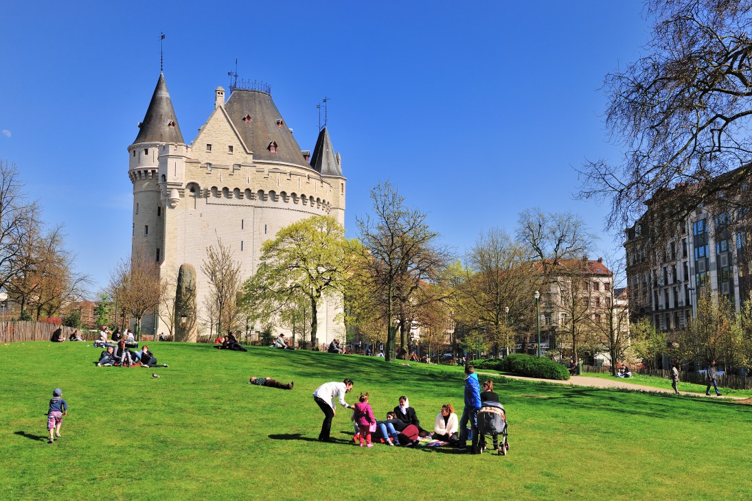 Families and visitors enjoying a sunny day on the grass at Hallepoort park with a medieval tower and historic buildings in the background.