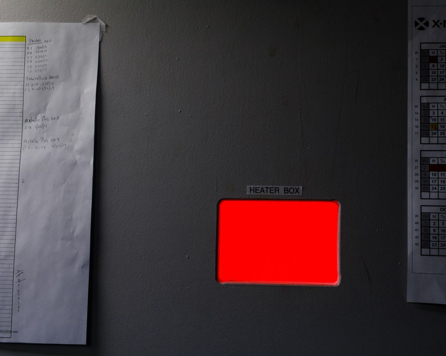 A red heating box labeled 'HEATER BOX' mounted on a gray wall with papers and calendars nearby.