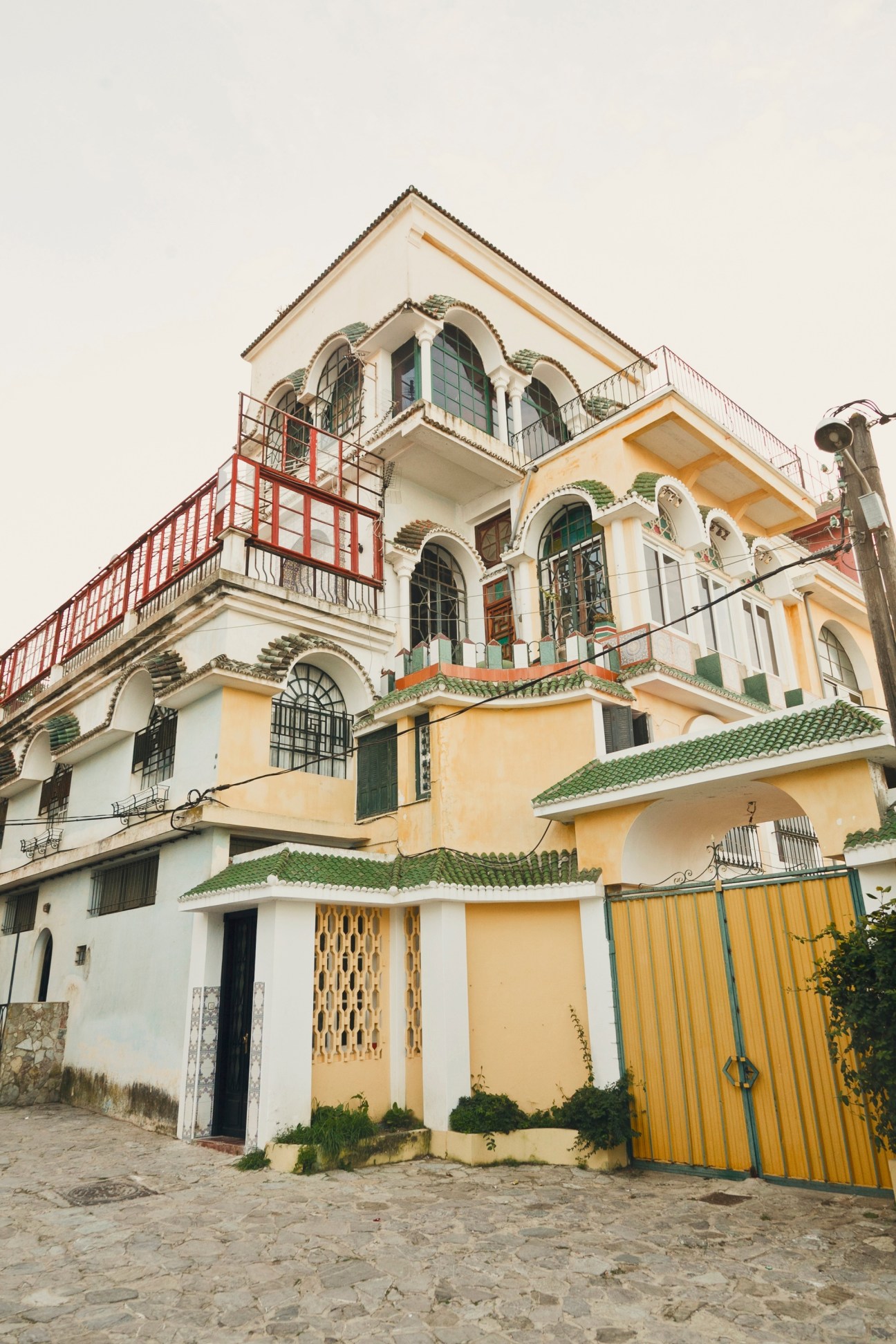 Colorful colonial building with arched windows, green tile roof details, and red metalwork railings in Marshan, Tangier.