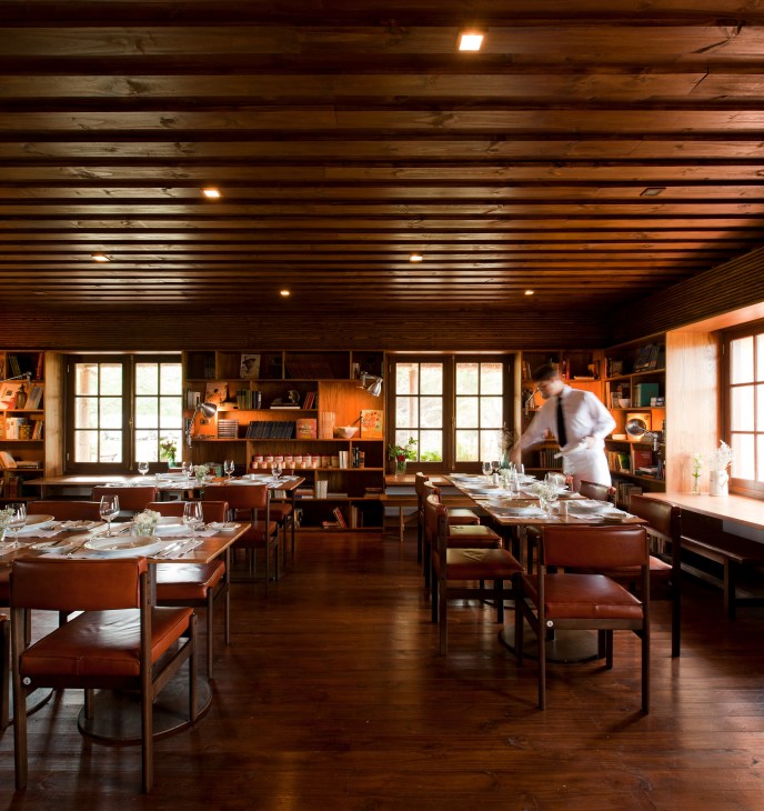 A waiter sets tables in Las Piedras restaurant with wood-panelled walls and shelving.