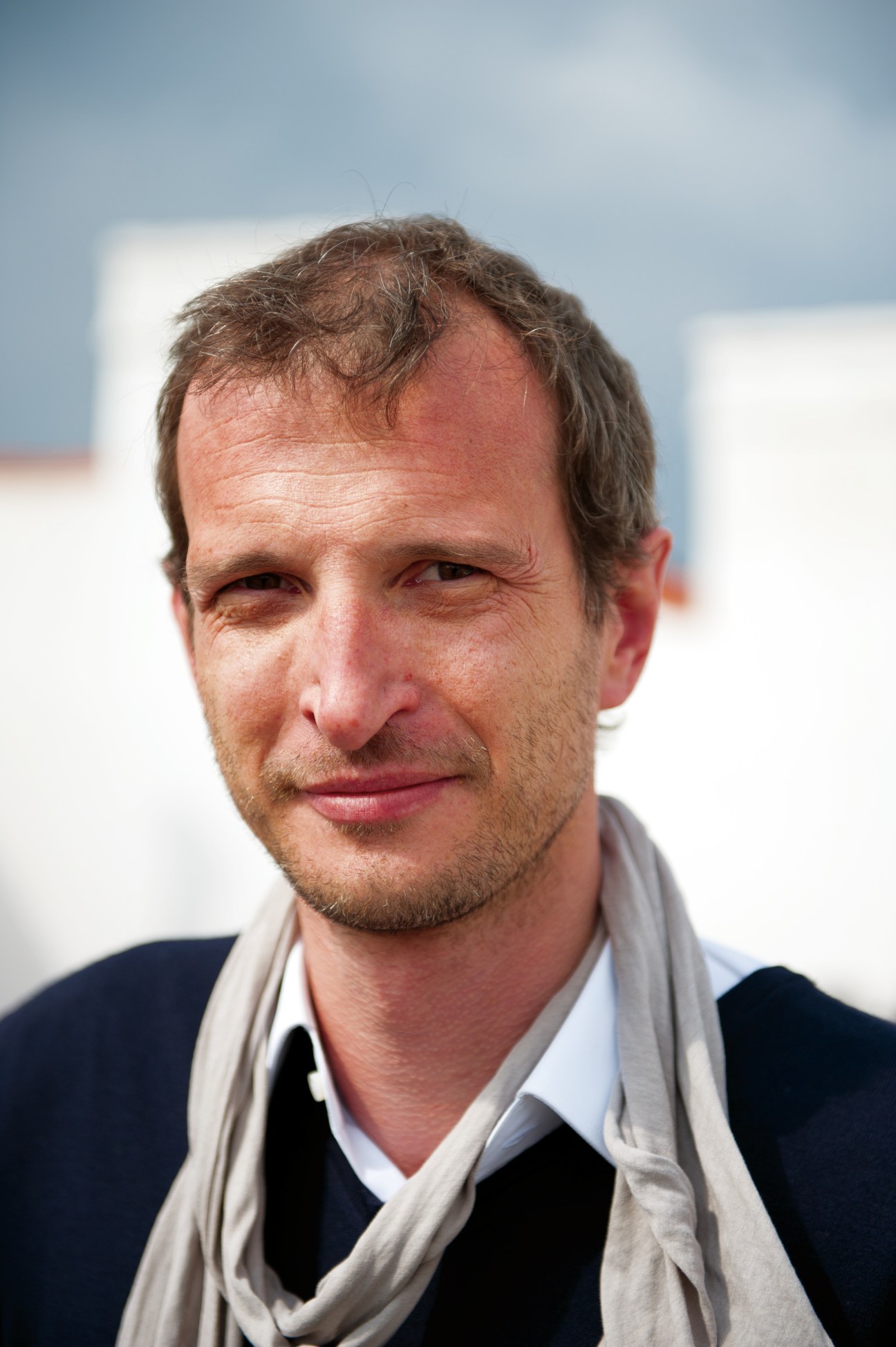 Portrait of Markus Huber, a man with receding brown hair wearing a dark jacket and beige scarf against a blurred white background.