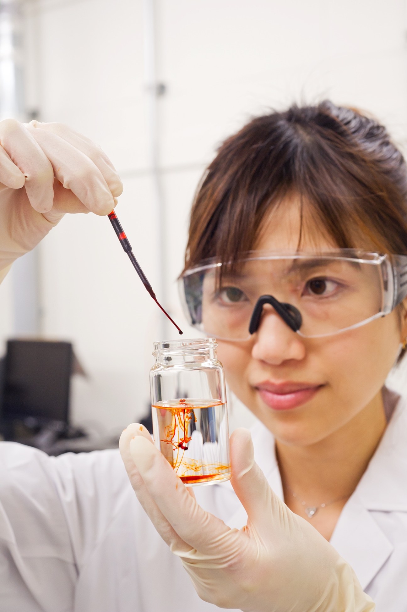 Laboratory technician in safety glasses mixing nanonized astaxanthin with water in a glass vial.