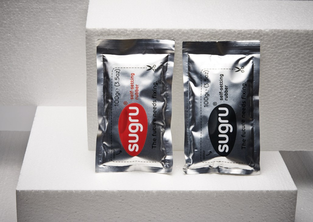 Two packets of Sugru self-setting rubber in red and black packaging displayed on a white platform.