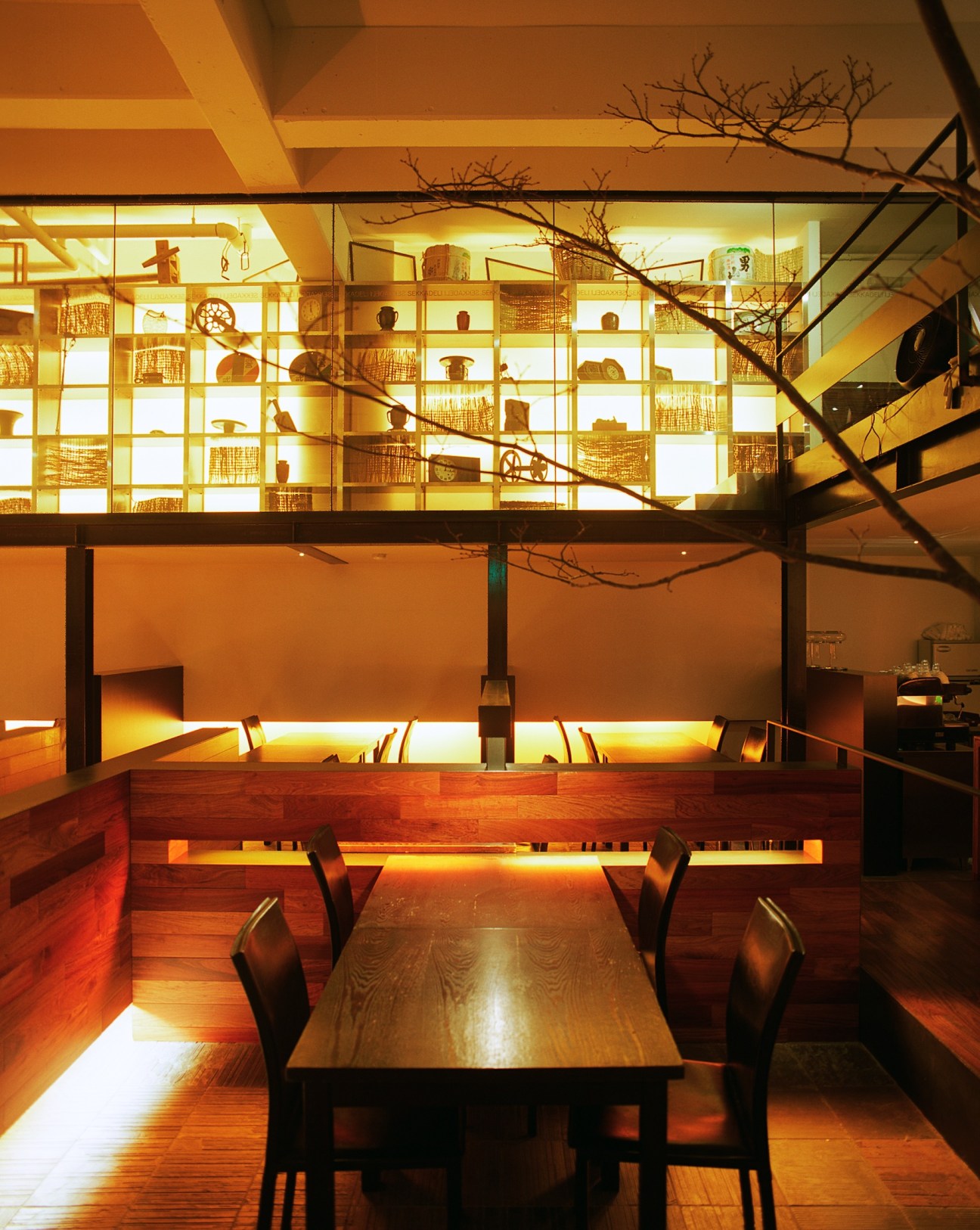 Modern dining room with wooden table, illuminated shelving displaying pottery, and warm amber lighting.