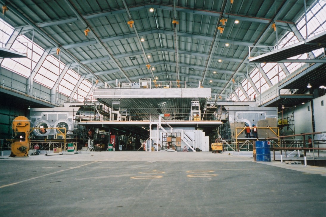 Interior of INCAT shipyard showing catamaran ferry under construction with overhead cranes and industrial infrastructure.