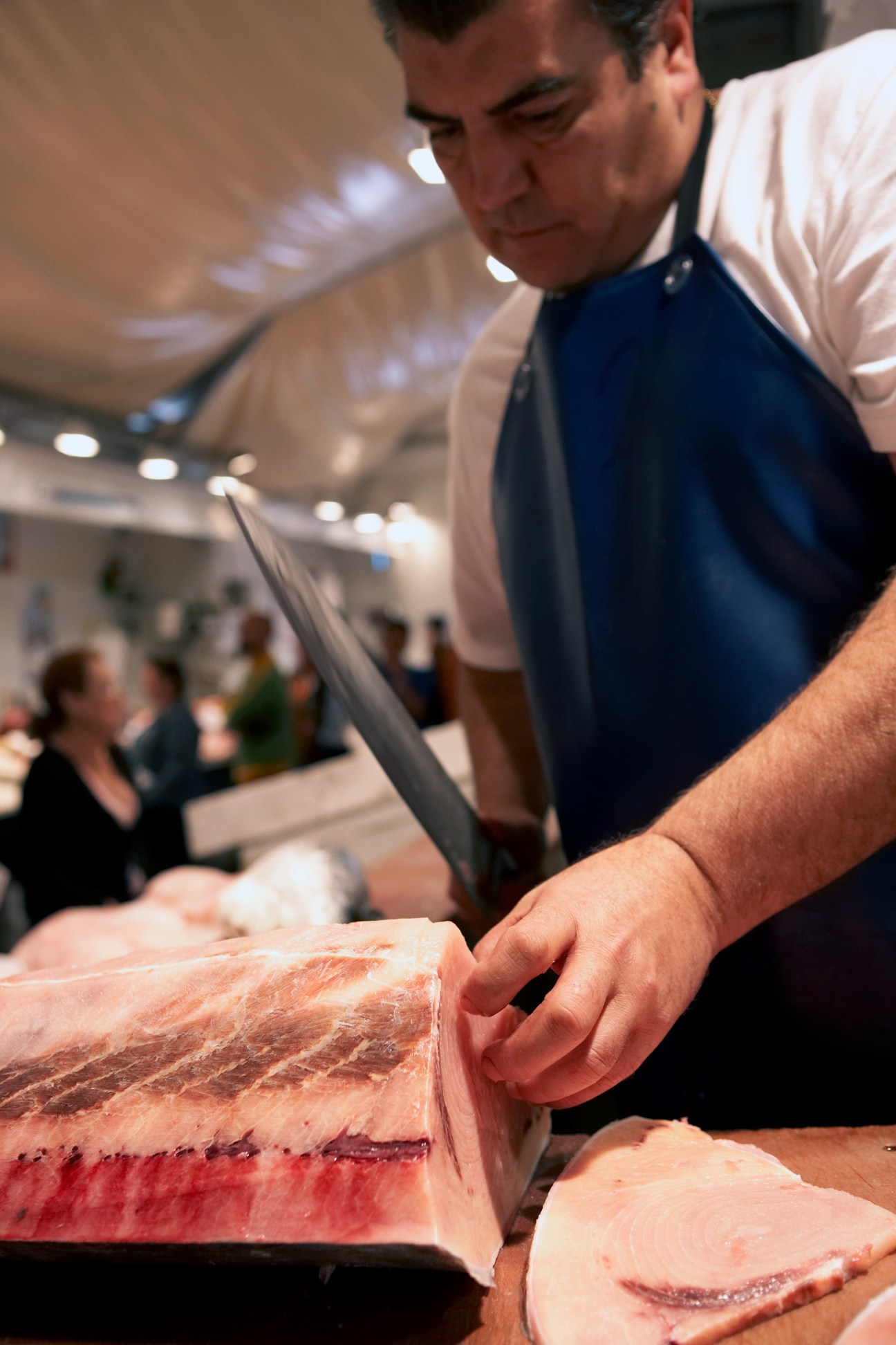 Fishmonger in blue apron butchering fresh fish at Cádiz market.
