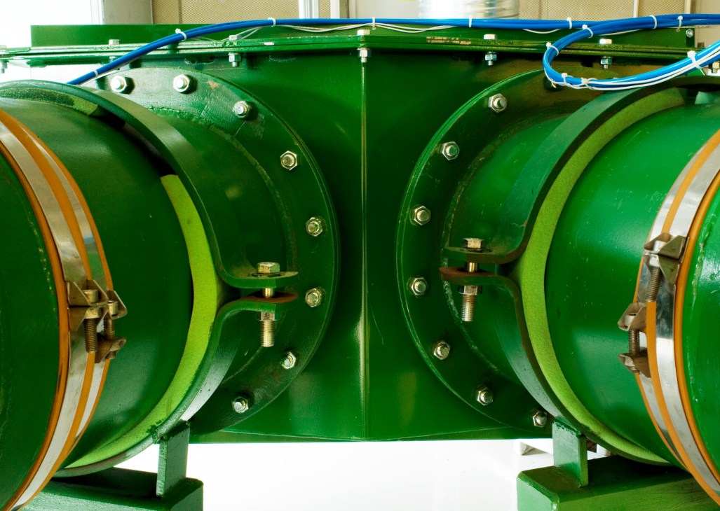 Green industrial waste separator machinery with blue pipes and metal fittings at a collection station.