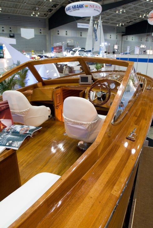 Interior of a vintage wooden Yamaha powerboat with white seats and steering wheel on display at a boat show.