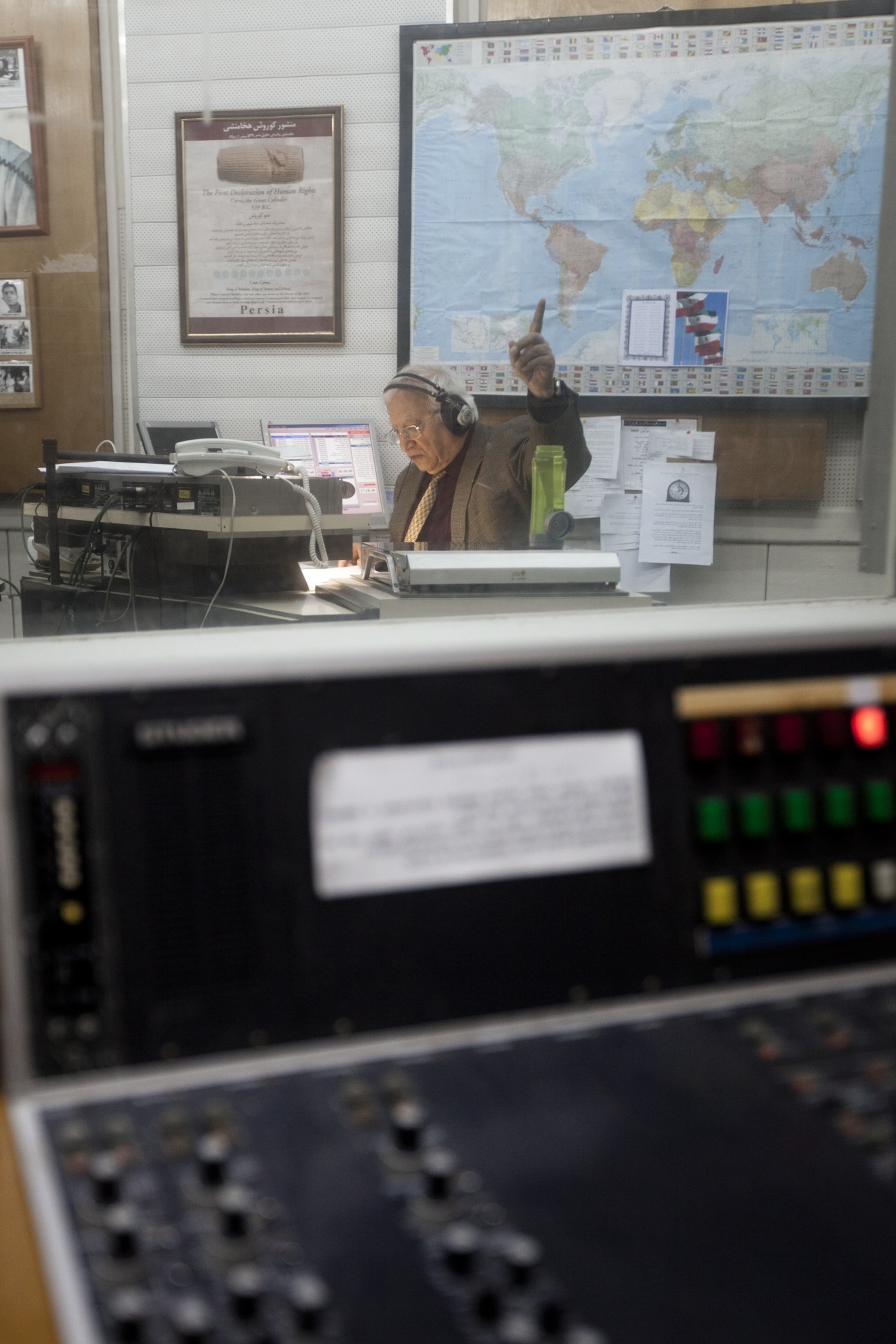 Menashe Amir gesturing while wearing headphones at a radio broadcast desk.