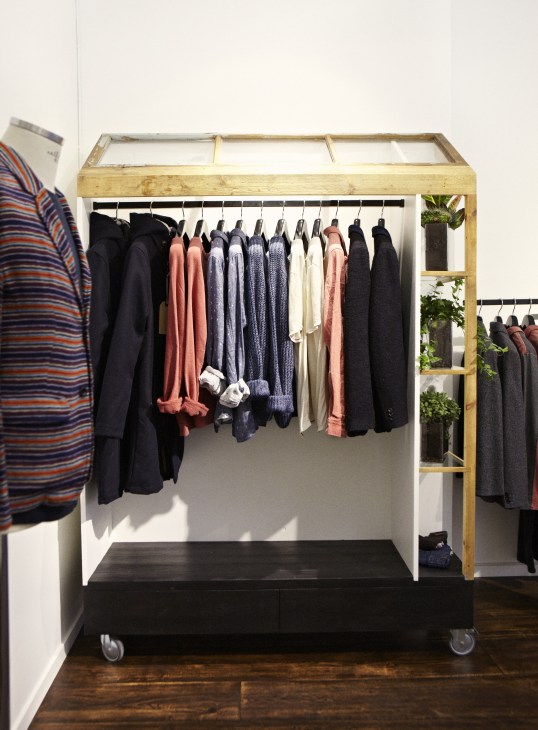 Uniforms for the Dedicated retail display in Södermalm with clothing on wooden frame and potted plants.