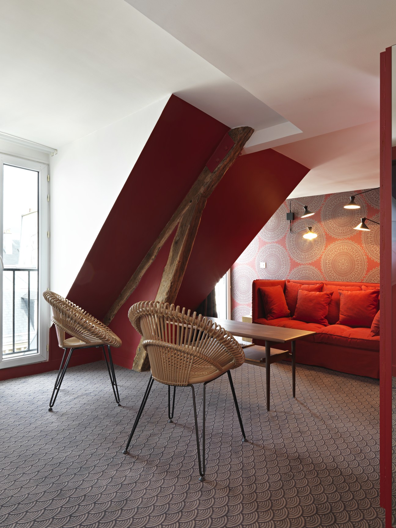 Modern hotel room with red accent walls, woven chairs, and geometric patterned carpet at Hotel Paradis in Paris.