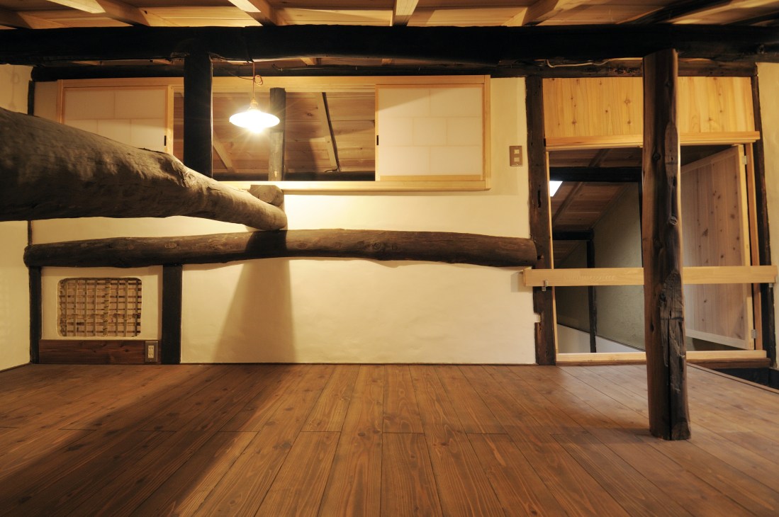 Interior of renovated Kyoto machiya showing wooden loft space with exposed beams and ventilation opening.