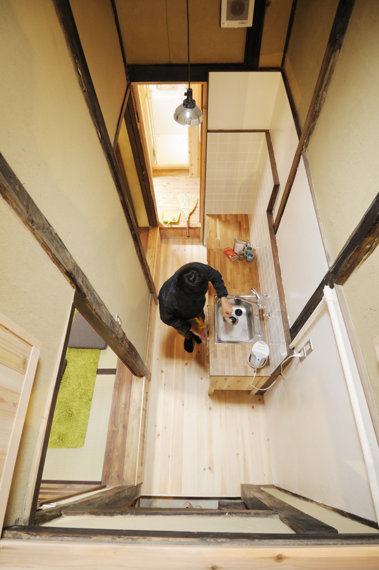 Overhead view of a renovated machiya kitchen with wooden beams, exposed rafters, and a person working below.