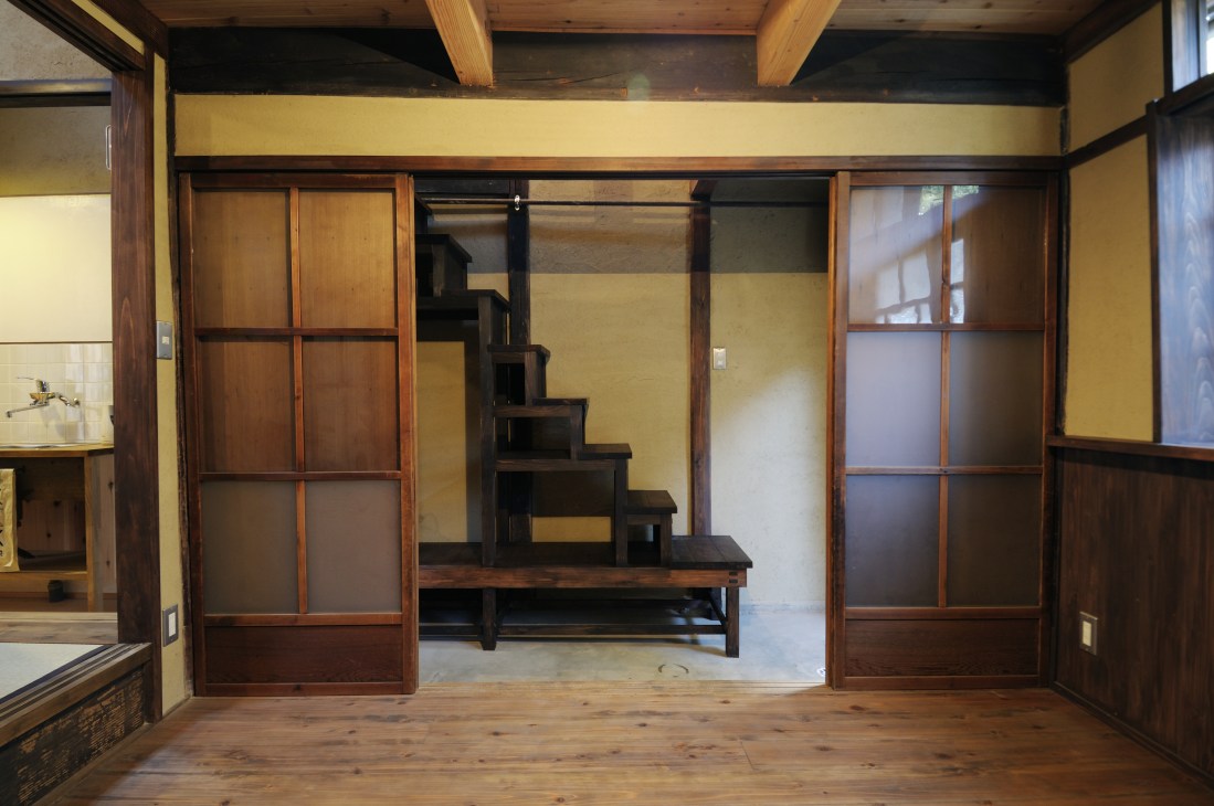 Traditional wooden interior with staircase doubling as storage beneath yellow walls and exposed beams.