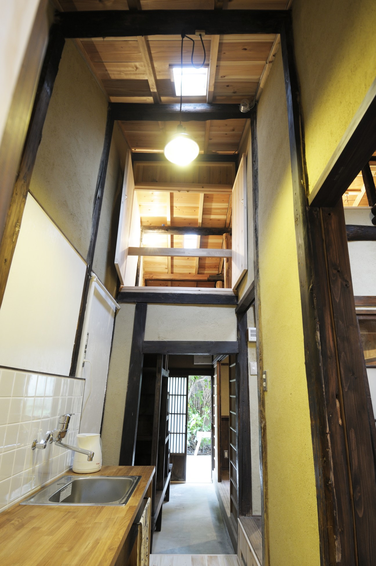 Narrow renovated kitchen in a Kyoto machiya with wooden countertops, skylight and exposed wooden ceiling beams.