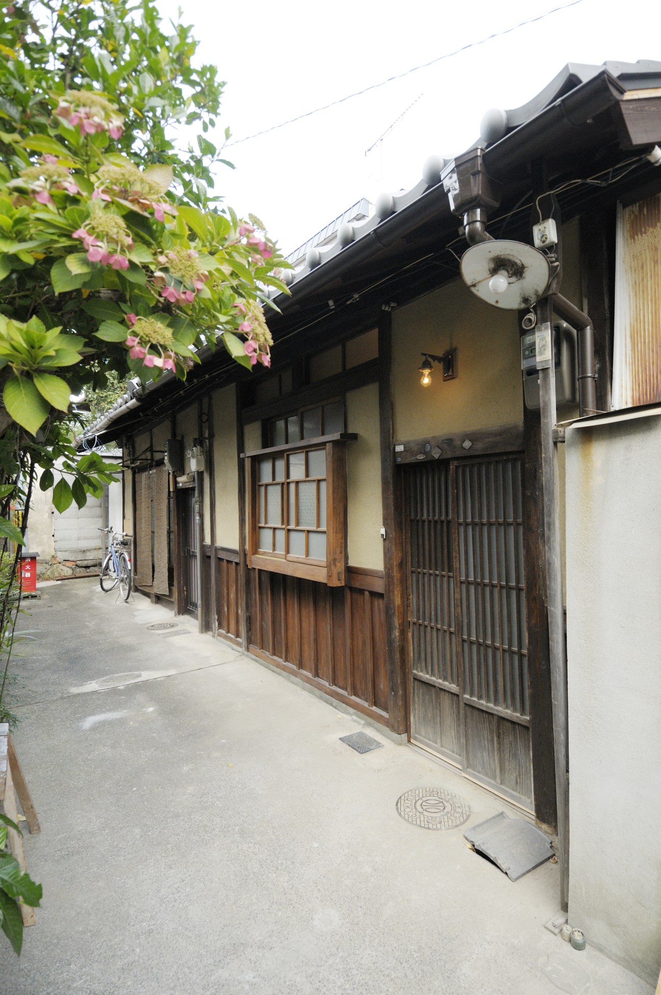 Traditional wooden machiya townhouse exterior in Kyoto with dark wooden doors, latticed windows, and pink flowering vine.