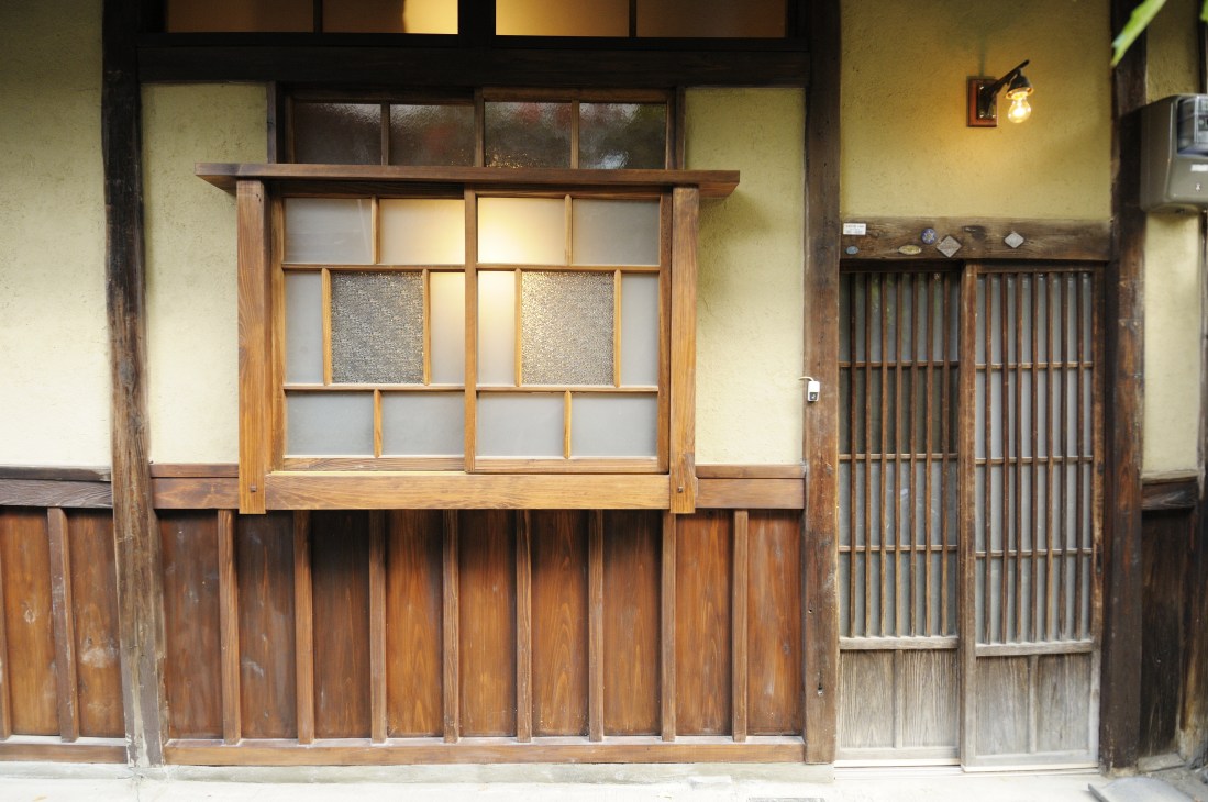 Traditional wooden machiya storefront with multilayered windows, wooden lattice screens and cream-colored plaster walls in Kyoto.
