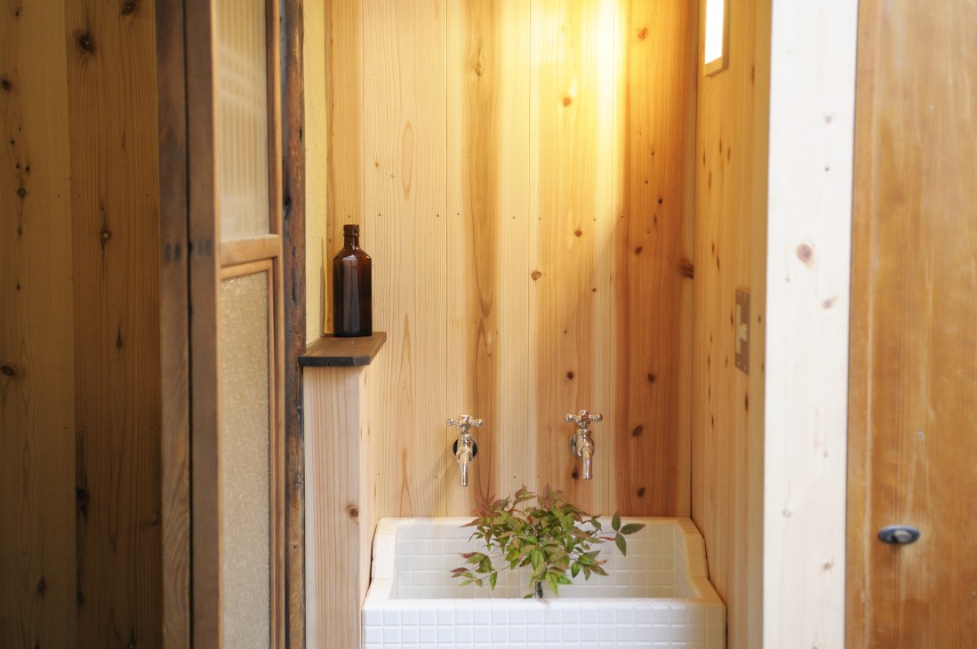 Modern bathroom with natural wood paneling, white tile sink, and minimalist chrome fixtures in renovated machiya townhouse.