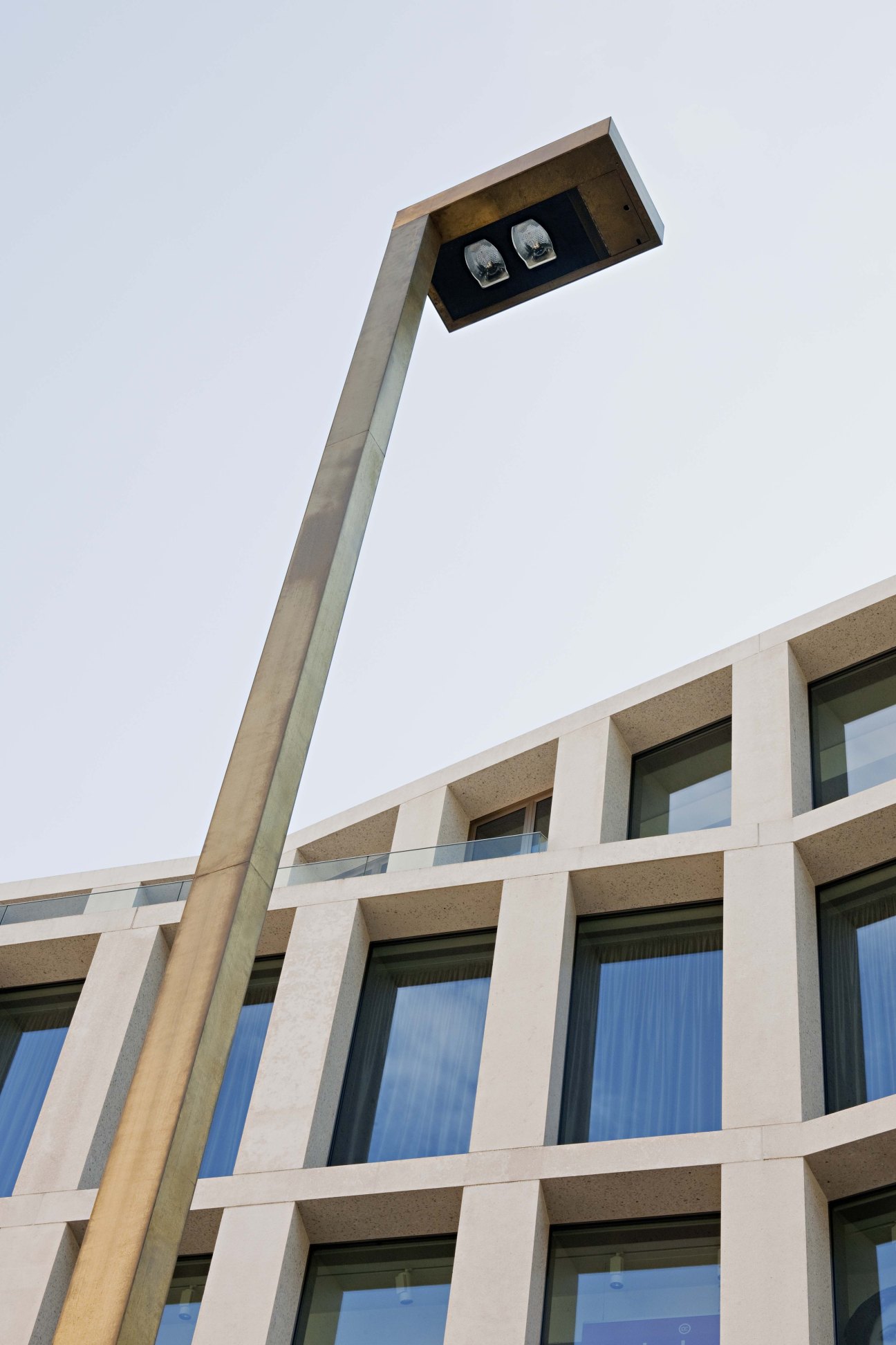 Modern streetlight with angled concrete pole and two lights mounted above a multi-story building facade.