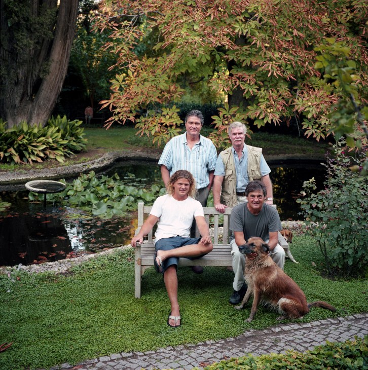 Brian and Mark Giraud with cousins Philip Whittall and Marten Steimbucher posing in a garden with a pond and dog.