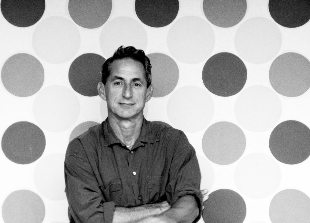 Black and white portrait of Mark McDonald, mid-century antiques dealer, against a patterned backdrop of circles.