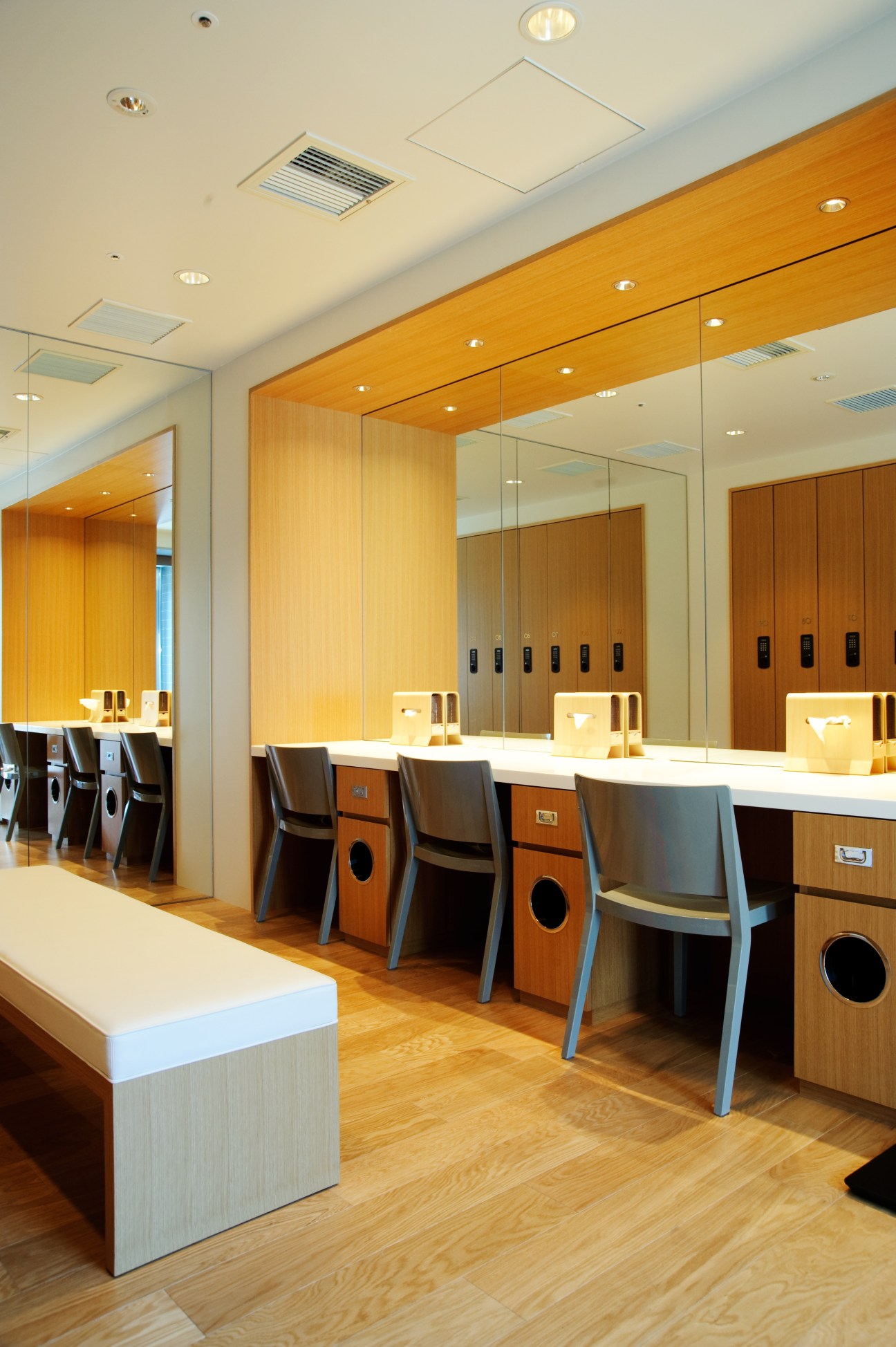 Modern locker room with wooden lockers, mirror-lined walls, and contemporary seating at the Soho spa in Tokyo.