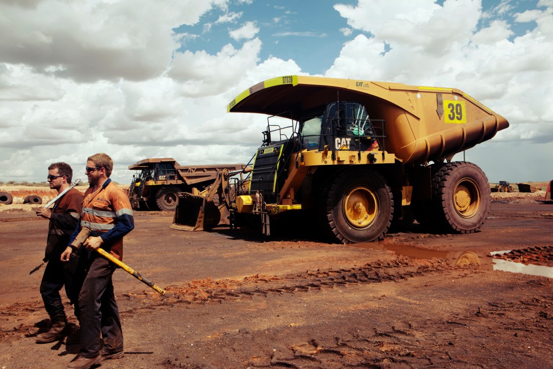 Two mechanics in high-visibility work clothing walk past a large yellow CAT haul truck at Woodie Woodie mining camp.
