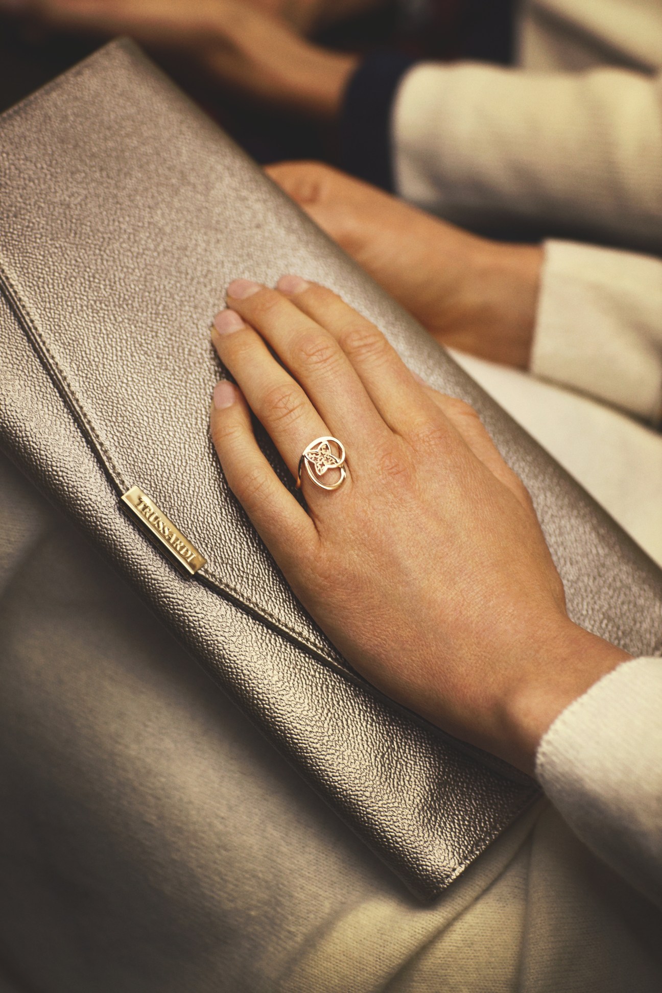 Close-up of a hand wearing a Louis Vuitton ring on a textured grey Trussardi clutch bag.