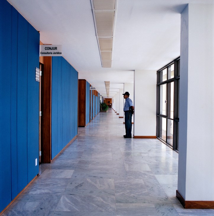 A security guard stands in a long corridor with bright blue wall panels and marble flooring in the Itamaraty Palace annex.