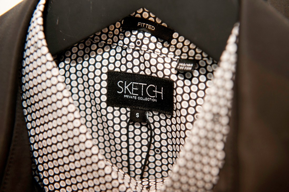 Close-up of a Sketch Private Collection clothing label on a garment with dotted mesh fabric.