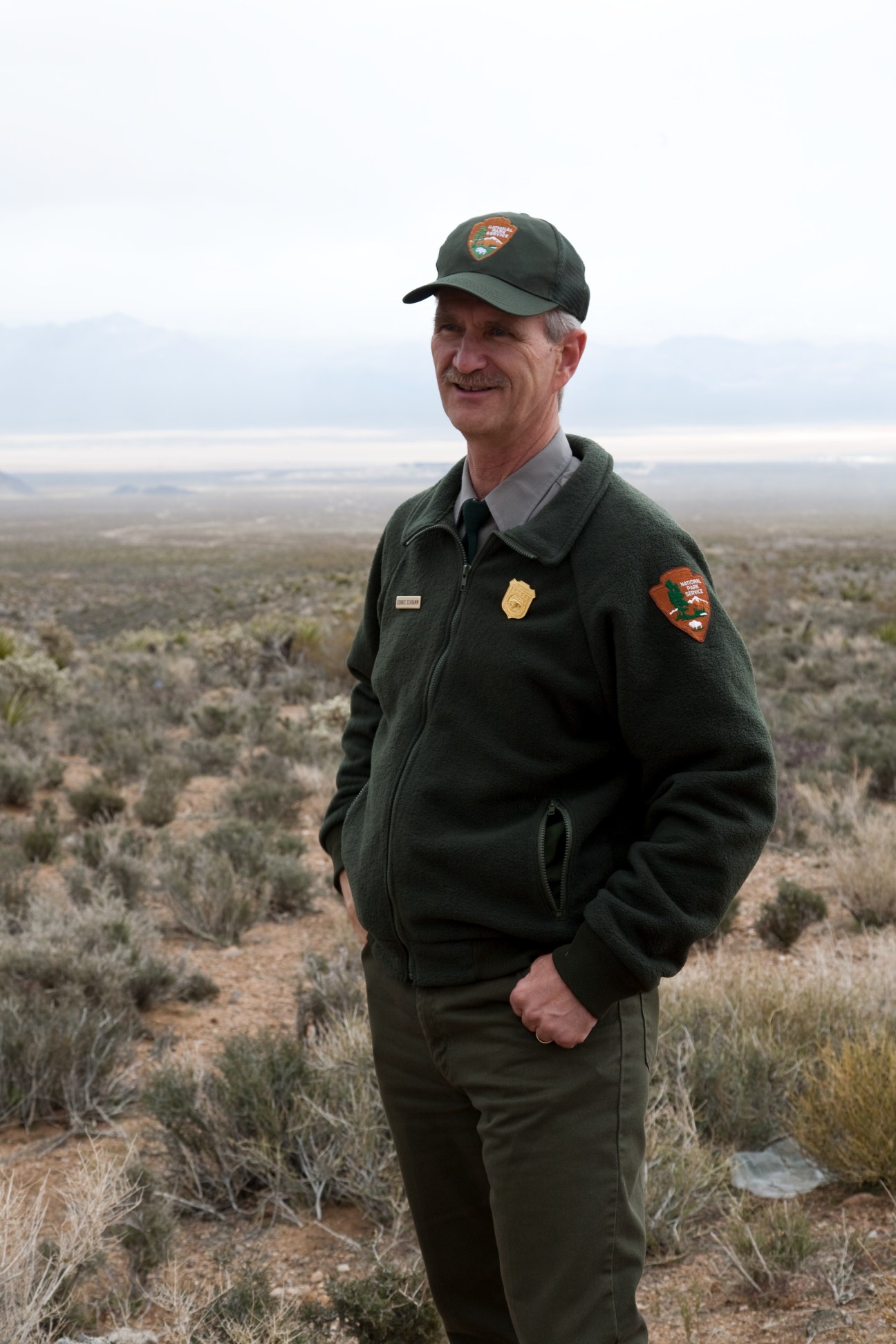 Dennis Schramm, superintendent of Mojave National Preserve, stands in desert landscape wearing National Park Service uniform.