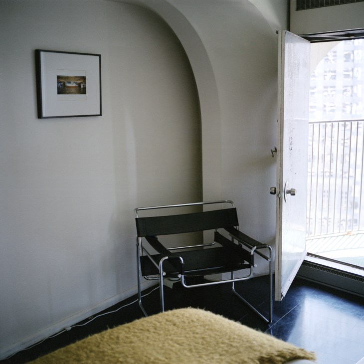 Marina City apartment interior with curved wall, black modern chair, and balcony door opening to city view.