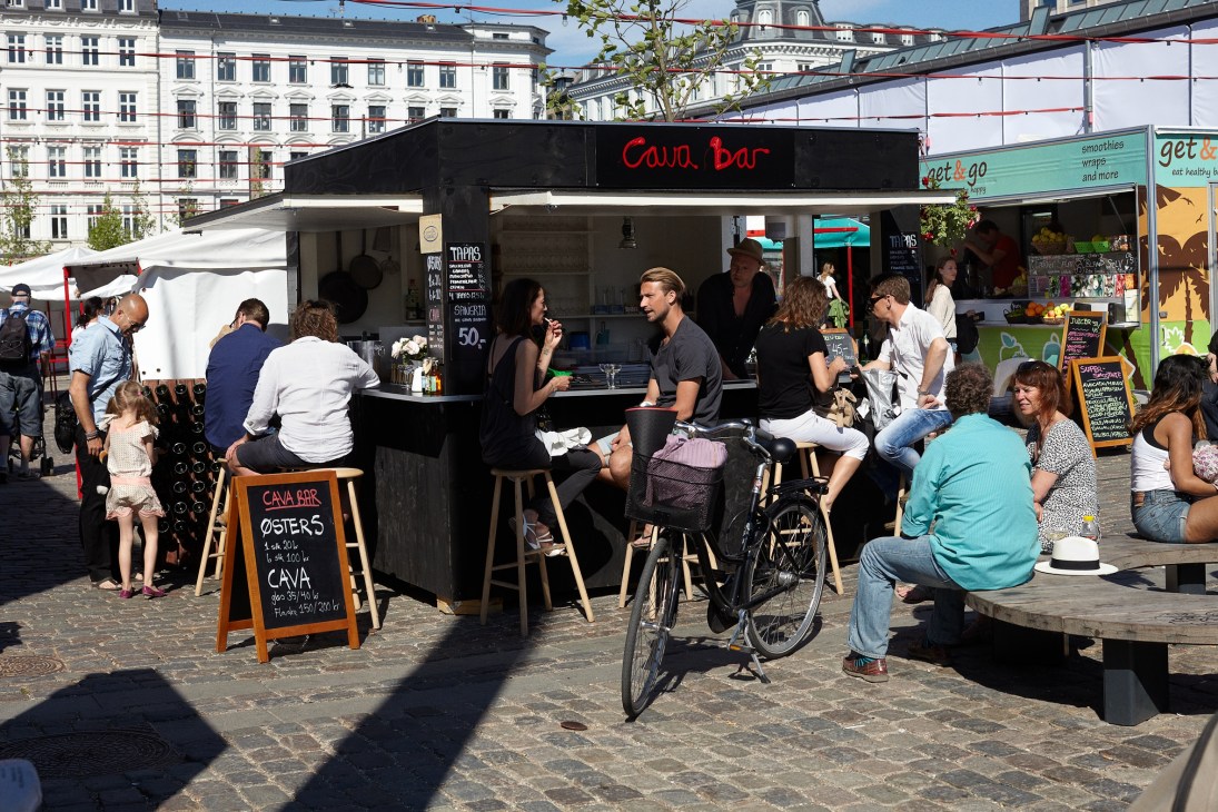 Outdoor food market with Cava Bar vendor and customers dining in Copenhagen square.