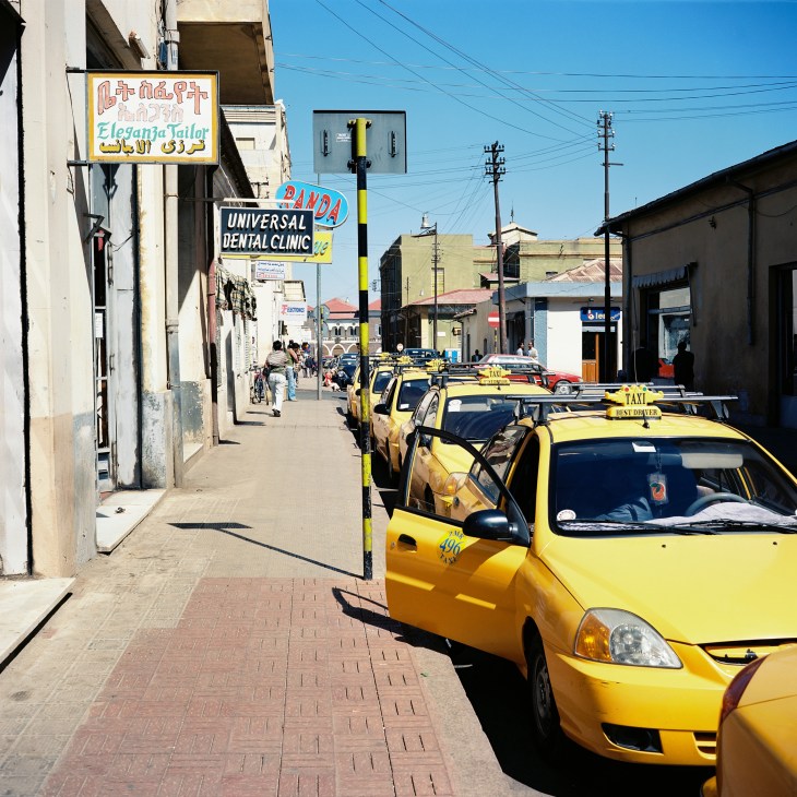 Yellow taxis line a street in Asmara with shop signs and pedestrians visible in the background.