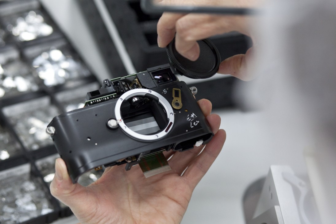 Hands holding a disassembled Leica camera showing its internal mechanics and lens mount.