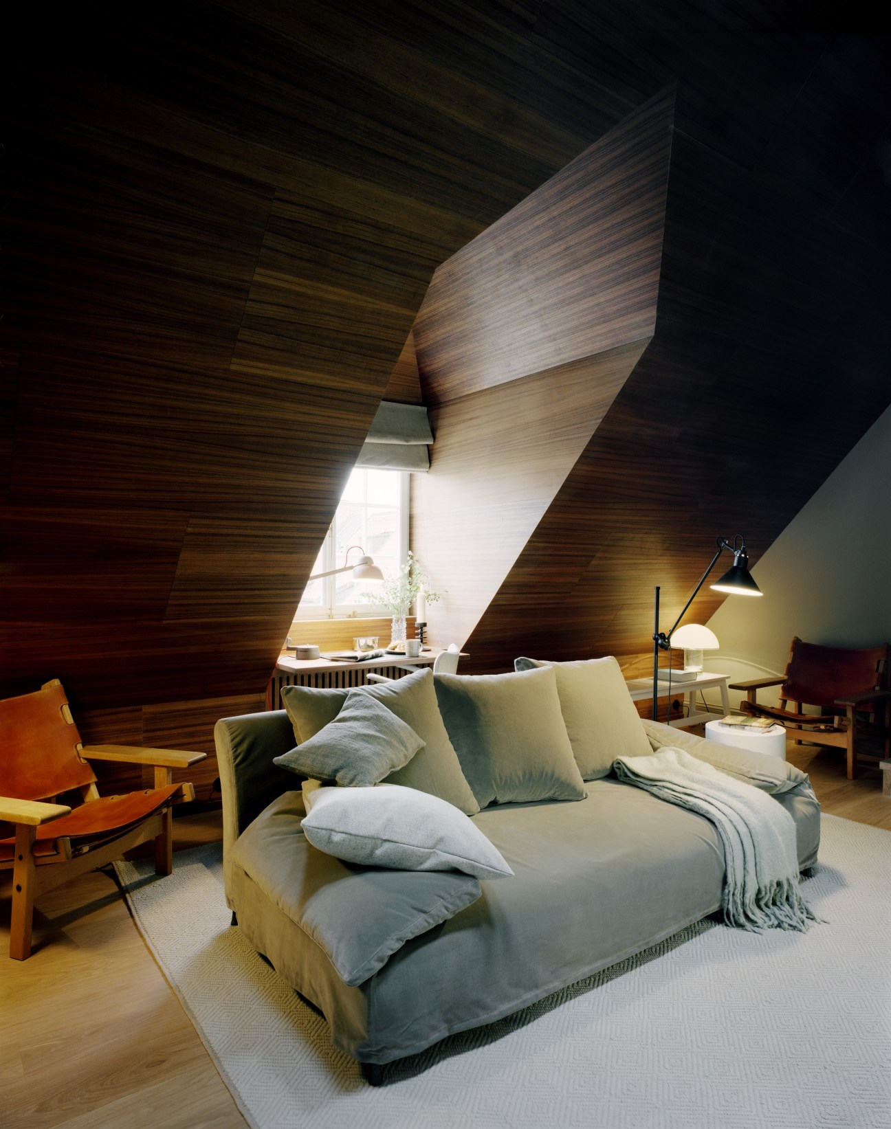 Ett Hem Hotel bedroom with wood-paneled angled ceiling, upholstered bed with pillows, and mid-century furniture.